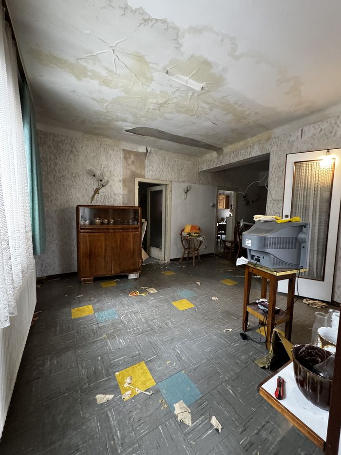 Dasselbe Wohnzimmer im Bestand mit Wasserschaden an der Decke und alten Bodenplatten